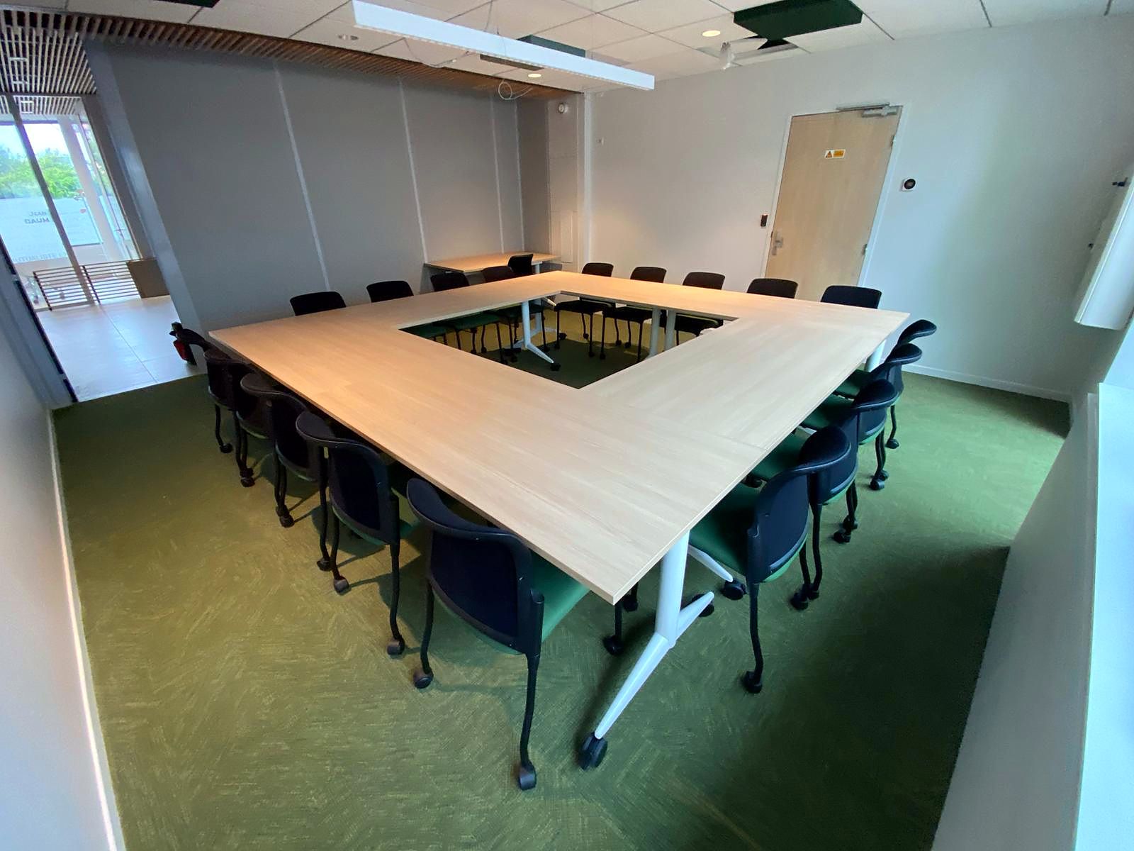 Salle de formation en U livrée par TEC’OFFICE : tables assemblées en carré ouvert, sièges noirs, moquette verte